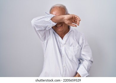 Senior Man With Grey Hair Standing Over Isolated Background Covering Eyes With Arm Smiling Cheerful And Funny. Blind Concept. 