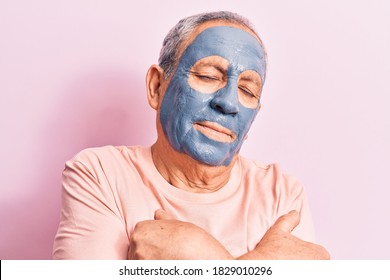 Senior Man With Grey Hair Wearing Mud Mask Hugging Oneself Happy And Positive, Smiling Confident. Self Love And Self Care 