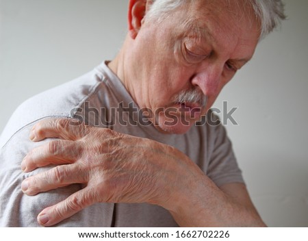 Senior man grips his shoulder in pain with room for text
