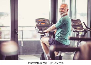 Senior Man At Gym Driving Bike And Looking At Camera.