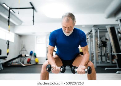 Senior Man In Gym Working Out With Weights, Squatting.