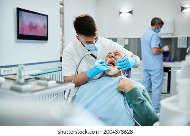 Senior Man Having Dental Drill Procedure During Appointment At Dentist's Office.