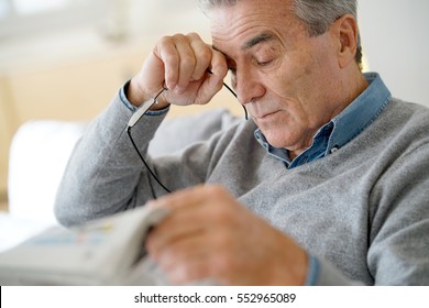 Senior man having a headache reading newspaper
