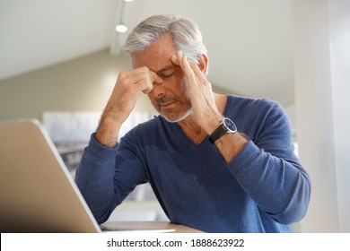 Senior man having a headache while working on laptop computer