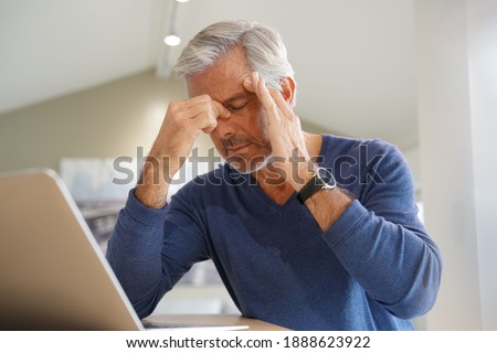Senior man having a headache while working on laptop computer