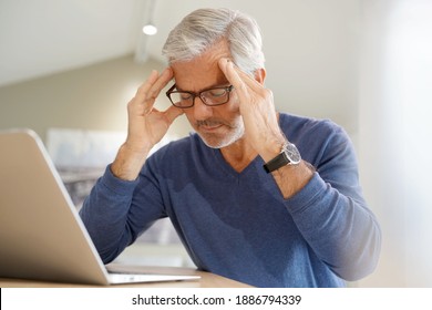 Senior man having migraine while working on laptop computer