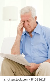 Senior Man Having Trouble With Eyesight While Reading A Newspaper At Home