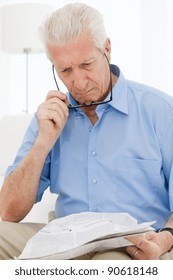 Senior Man Having Trouble With Eyesight While Reading A Newspaper At Home