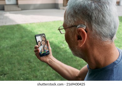 Senior man with a hearing aid behind the ear communicates with his family via video communication via a smartphone. Full human life with hearing aids - Shutterstock ID 2169430425