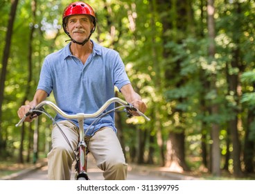 Senior man in helmet is riding bicycle in park.