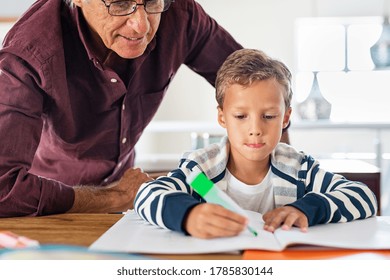 Senior man helping child to complete his homework at home. Focused school boy preparing project on notebook with grandparent. Grandson and grandfather writing exercise on paper. - Powered by Shutterstock