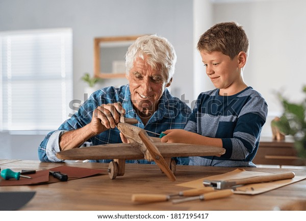 Senior man helping child to screw an airplane\
part that they are building together during summer vacation.\
Retired grandfather helping grandson in making wooden plane at home\
for school project.