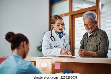 Senior man and his doctor going through medical data at reception desk at at the clinic. - Shutterstock ID 2256286039