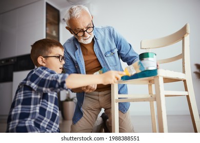 Senior Man And His Grandson Painting Wooden Chair In Blue Color At Home.