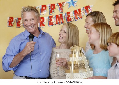 Senior Man In His Honor Giving Speech At Retirement Party With Arms Around Wife By Family