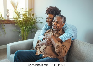 Senior man and his middle aged daughter smiling at each other embracing, close up. Portrait of a daughter holding her elderly father, sitting on a bed by a window in her father's room. - Powered by Shutterstock