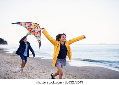 Senior man and his preteen granddaughter playing with kite on sandy beach.