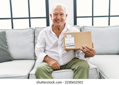Senior man holding delivery package at home looking positive and happy standing and smiling with a confident smile showing teeth  - Shutterstock ID 2230652501