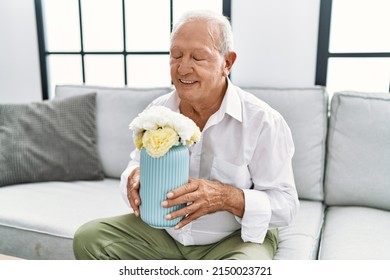 Senior Man Holding Flower Pot Sitting On Sofa At Home