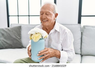 Senior Man Holding Flower Pot Sitting On Sofa At Home