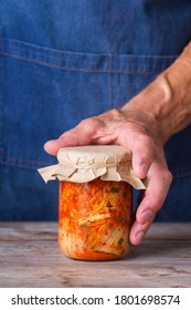 Senior Man Holding In Hands Homemade Organic Traditional Korean Kimchi Cabbage Salad In A Glass Jar On A Wooden Table. Fermented Vegetarian, Vegan Preserved Gut Health Food Concept