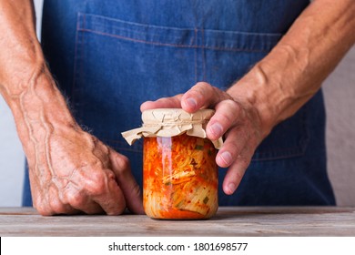 Senior Man Holding In Hands Homemade Organic Traditional Korean Kimchi Cabbage Salad In A Glass Jar On A Wooden Table. Fermented Vegetarian, Vegan Preserved Gut Health Food Concept