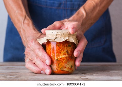 Senior Man Holding In Hands Homemade Organic Traditional Korean Kimchi Cabbage Salad In A Glass Jar On A Wooden Table. Fermented Vegetarian, Vegan Preserved Gut Health Food Concept