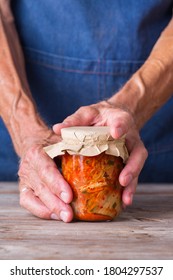 Senior Man Holding In Hands Homemade Organic Traditional Korean Kimchi Cabbage Salad In A Glass Jar On A Wooden Table. Fermented Vegetarian, Vegan Preserved Gut Health Food Concept