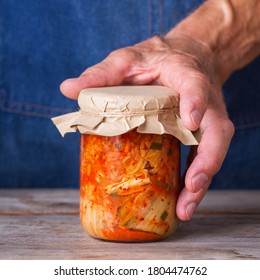 Senior Man Holding In Hands Homemade Organic Traditional Korean Kimchi Cabbage Salad In A Glass Jar On A Wooden Table. Fermented Vegetarian, Vegan Preserved Gut Health Food Concept