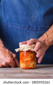 Senior Man Holding In Hands Homemade Organic Traditional Korean Kimchi Cabbage Salad In A Glass Jar On A Wooden Table. Fermented Vegetarian, Vegan Preserved Gut Health Food Concept