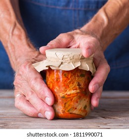 Senior Man Holding In Hands Homemade Organic Traditional Korean Kimchi Cabbage Salad In A Glass Jar On A Wooden Table. Fermented Vegetarian, Vegan Preserved Gut Health Food Concept