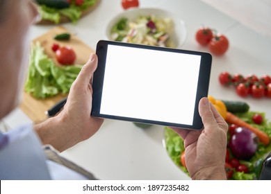 Senior Man Holding In Hands Using Tablet Computer Mockup Screen On Healthy Food Vegetable Background. Online Grocery Shopping Delivery App Ads Concept, Cook Book Diet Plan Recipes, Over Shoulder View.