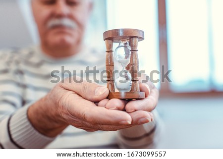 Senior man holding hourglass in retirement home, symbol for limited life span