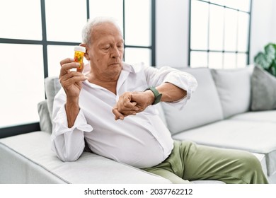 Senior man holding pills checking the time on wrist watch, relaxed and confident  - Powered by Shutterstock