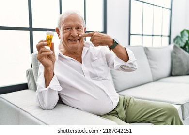 Senior Man Holding Pills Pointing With Hand Finger To Face And Nose, Smiling Cheerful. Beauty Concept 