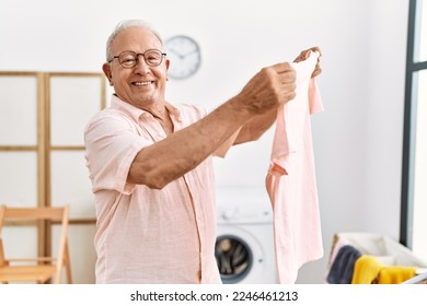 Senior man holding t shirt hanging clothes on clothesline at laundry room - Powered by Shutterstock