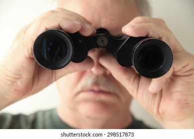 A Senior Man Holds An Old Pair Of Binoculars Pointed At The Camera.