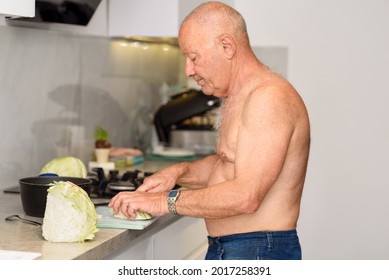 Senior Man At Home Is Cooking. Extreme Heat Summer, Shirtless Mature Man Inside Home In His Kitchen Trying To Cool Off And Prepares Vegetables.