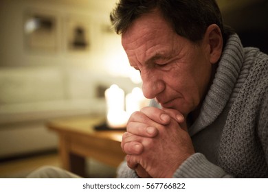 Senior man at home praying, burning candles behind him. - Powered by Shutterstock