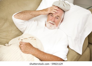 Senior Man Home Sick In Bed, With An Ice Pack On His Head.  Could Be Hangover Or Illness.