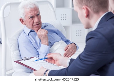 Senior man in a hospital bed about to sign his last will in the presence of the lawyer