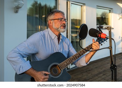 Senior man imposing musician plays the guitar and sings into microphone. Elegant elderly male 60 bearded performs outdoors in summer. Attractive handsome pensioner man activity creativity.
