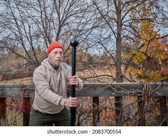 Senior Man (in Late 60s) Is Exercising With A Steel Mace In His Backyard, Fall Scenery