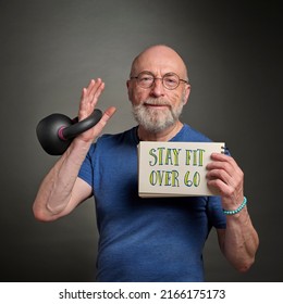 senior man (in late 60s) exercising with iron kettlebell and holding notebook sign - stay fit over 60, active senior and fitness concept