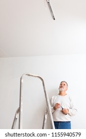 Senior man installing a ceiling light n a freshly renovated appartment