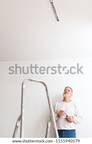 Senior man installing a ceiling light n a freshly renovated appartment