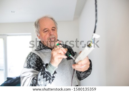 Senior man installing a ceiling light in a freshly renovated house; home handyman