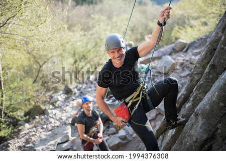 Senior man with instructor climbing rocks outdoors in nature, active lifestyle.