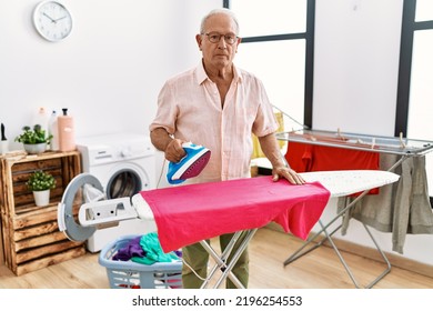 Senior Man Ironing Clothes At Home Thinking Attitude And Sober Expression Looking Self Confident 