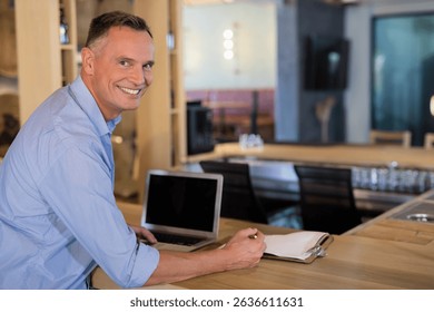 Senior man leaning on wooden bar counter at café lounge using laptop and writing on clipboard. Urban, workspace, modern, relaxation, professional, cozy, ambient